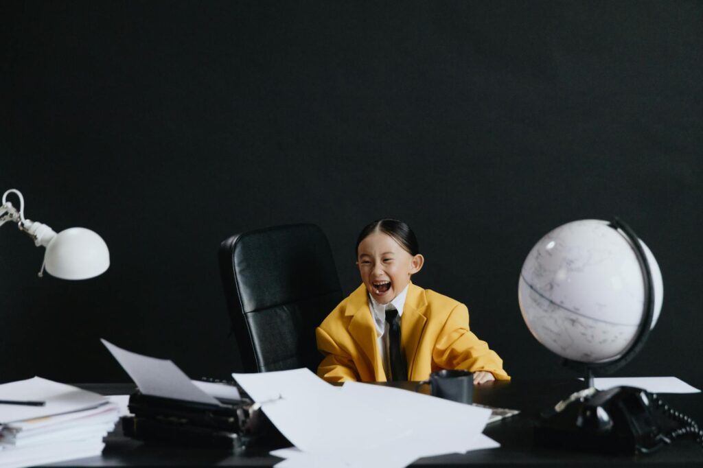 Adorable child in yellow suit laughing at office desk with globe and papers.