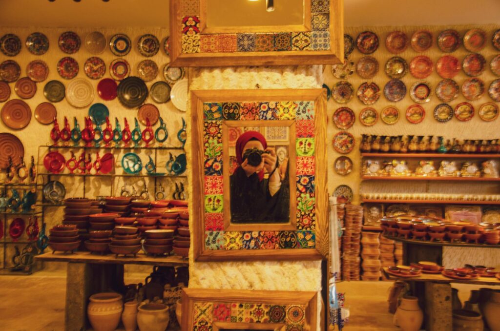 Vibrant pottery shop interior with diverse ceramics reflecting in a mirror.