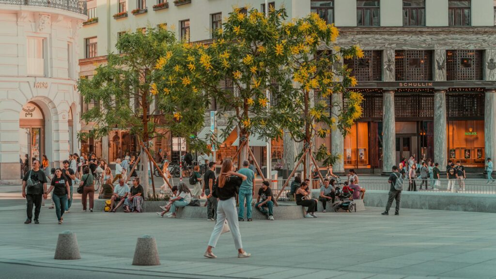 People relaxing in a bustling urban square surrounded by greenery.