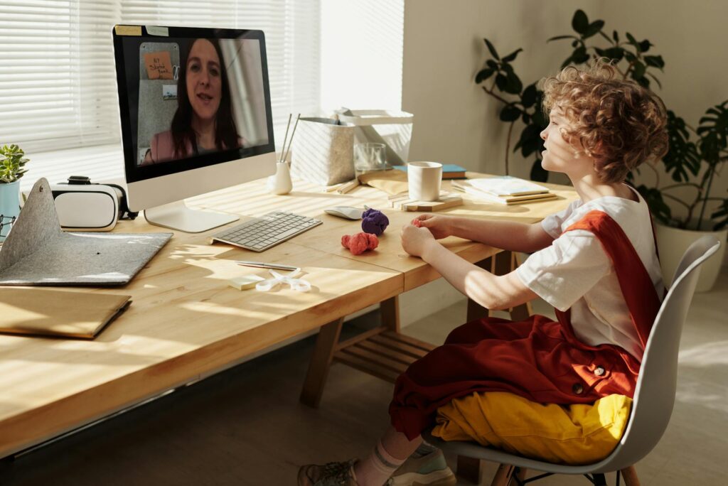 Young child using computer for distance learning with crafts on a table.