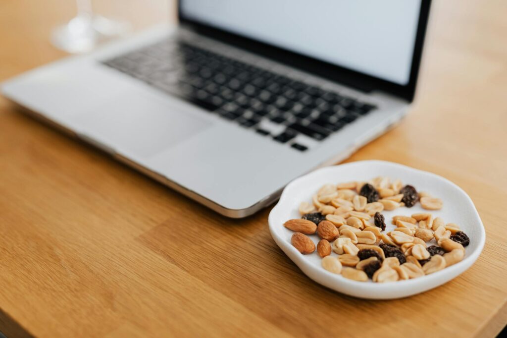 A plate of mixed nuts beside a laptop on a wooden desk, perfect for remote work inspiration.