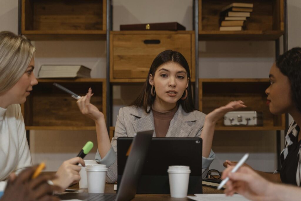 Three women engaged in a collaborative meeting with laptops and notes in an office setting.