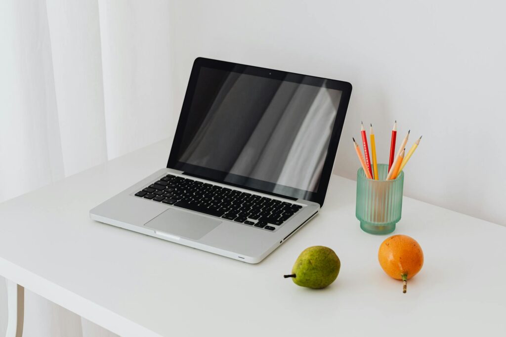 A clean and modern workspace featuring a laptop, colorful pencils, and fresh fruits on a white desk.