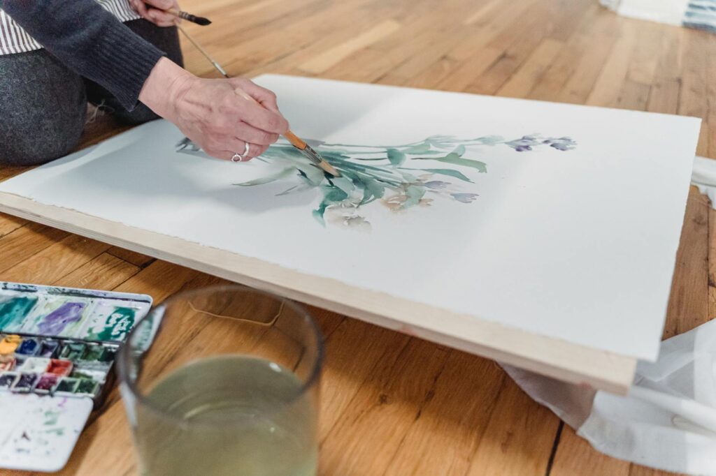 Artist creating a botanical watercolor painting indoors with vibrant palette and brush.