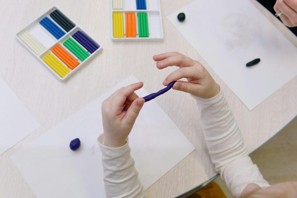 Overhead view of a child shaping purple modelling clay, surrounded by colorful clay sticks.