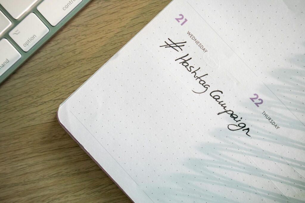 Open planner with 'Hashtag Campaign' handwritten next to keyboard. Ideal for social media and productivity themes.