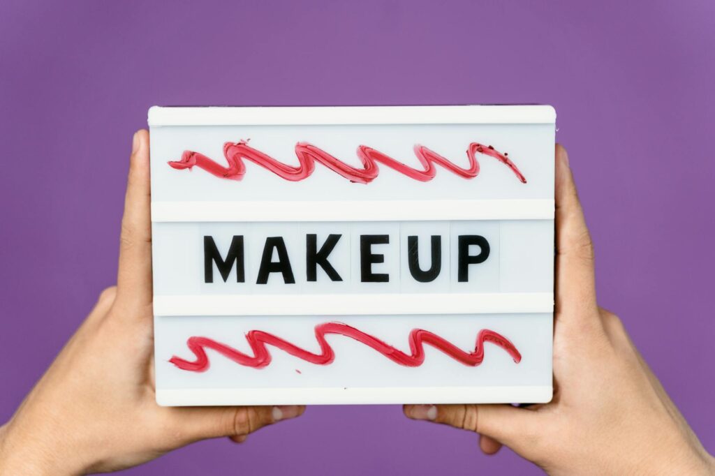 Close-up of a lightbox with the word 'MAKEUP' held by hands, featuring artistic red swirls.