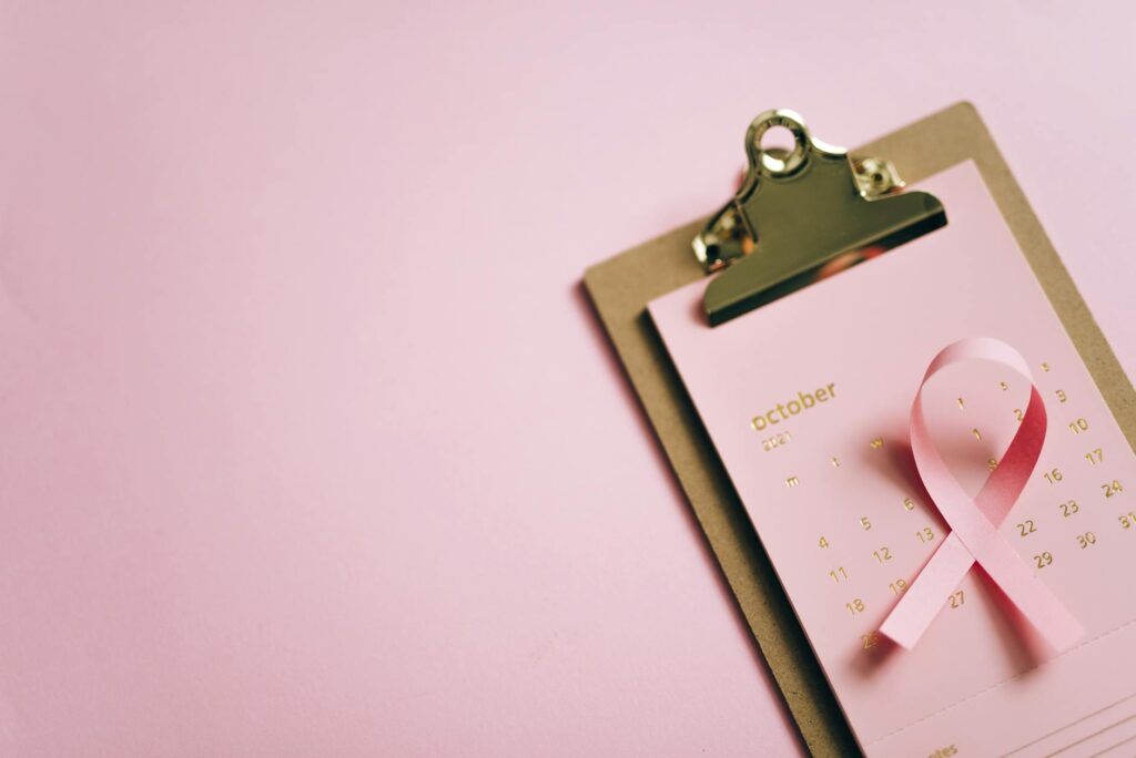 An overhead shot of an October calendar with a pink ribbon on a clipboard, symbolizing breast cancer awareness.