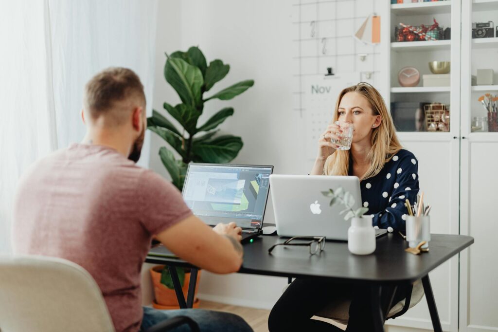 Two colleagues working in a stylish office space with laptops and beverages.