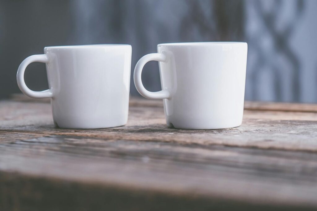 Close-up of two white ceramic cups on a rustic wooden table, featuring soft natural light.