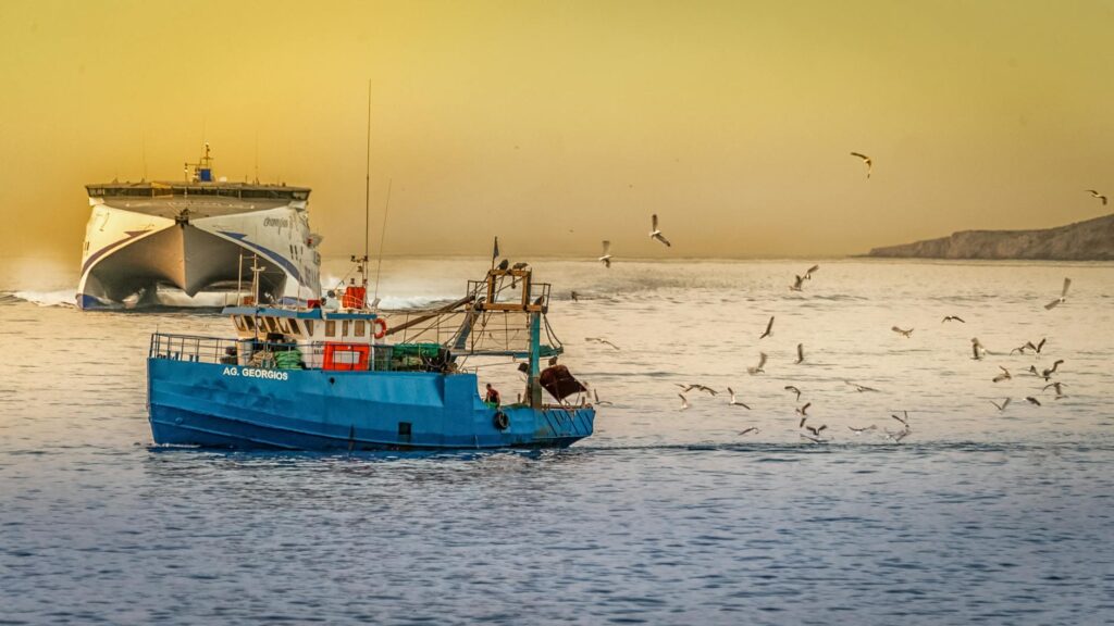 Fishing boats and seagulls in Rethymno, Greece at sunset with a ferry in the background.