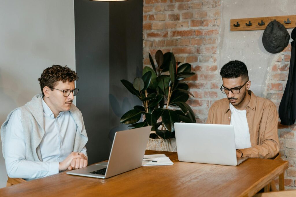 Two professionals collaborating in a stylish office setting with laptops and a potted plant.